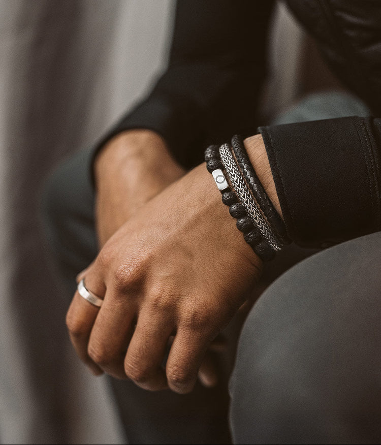 Gros plan sur le poignet d'une personne portant des bracelets et une bague, vêtue d'une veste noire.
