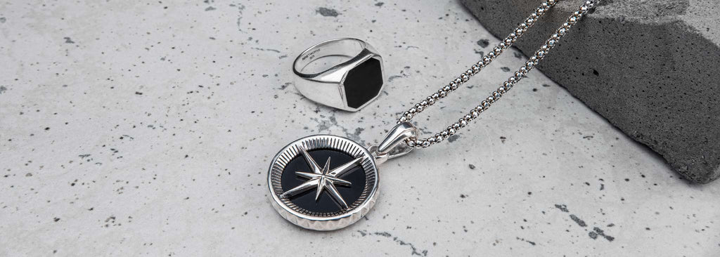 A silver necklace with a black compass, suitable for men.