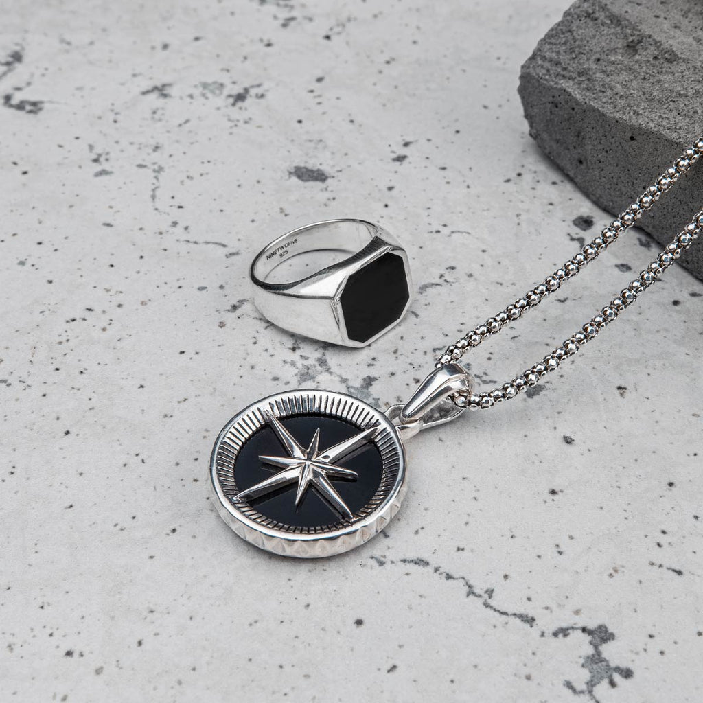 A silver compass necklace and mens silver ring set.