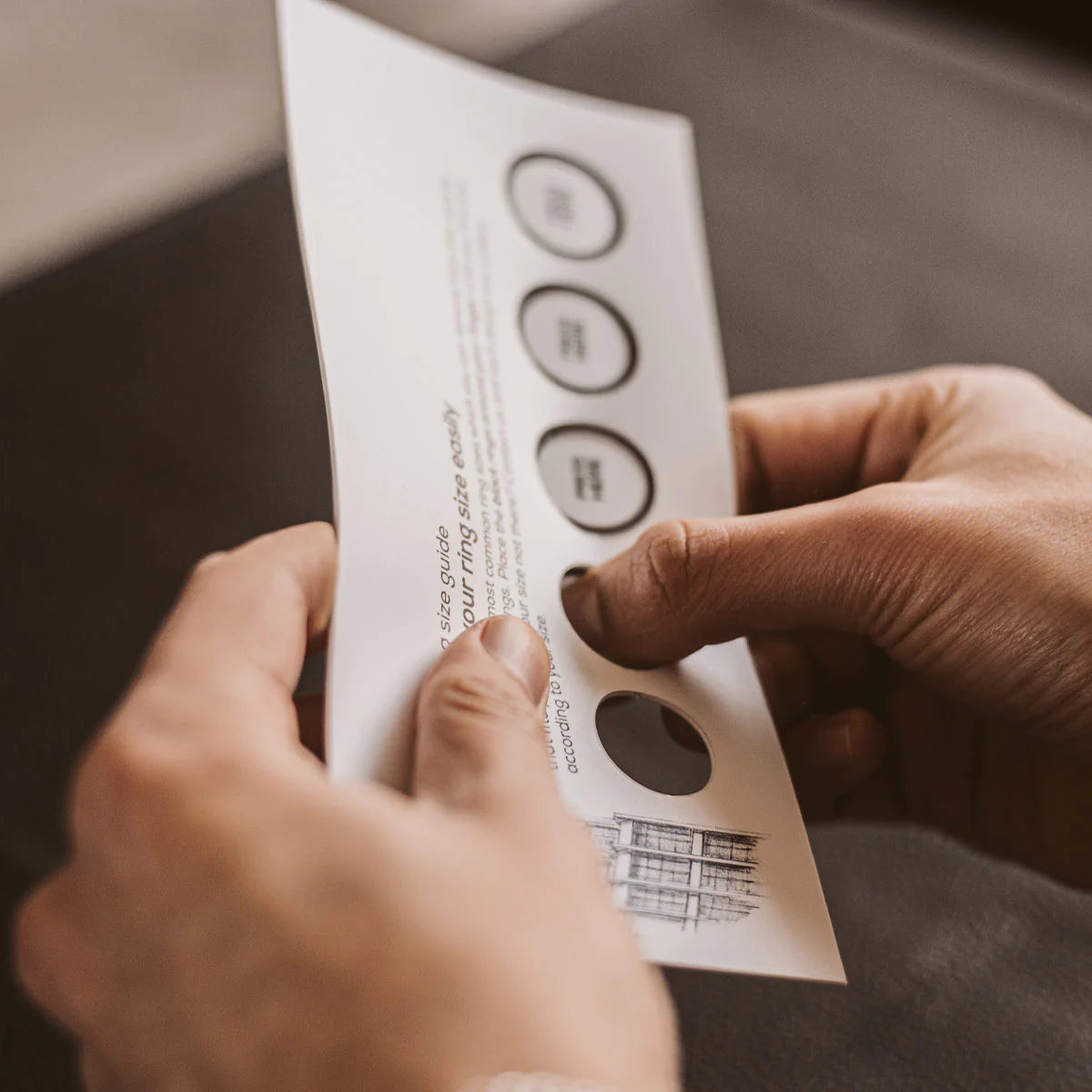 A person is holding a mens ring size chart paper.