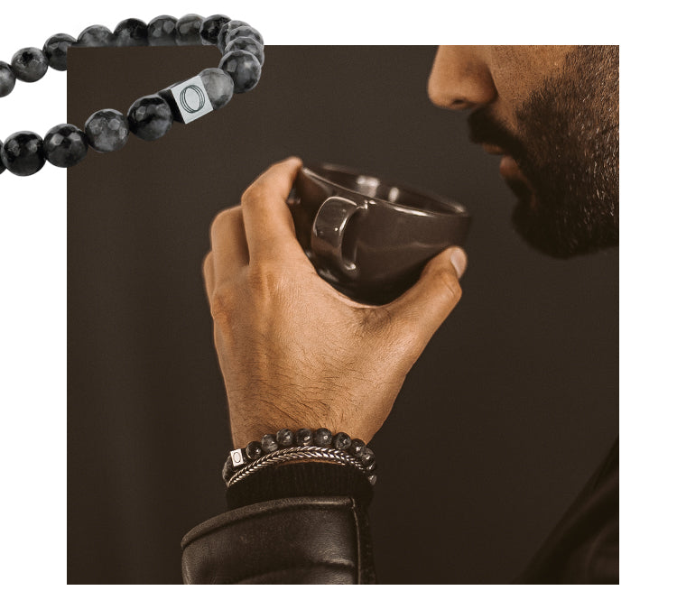 A man is holding a cup of coffee while wearing a black beaded bracelet.
