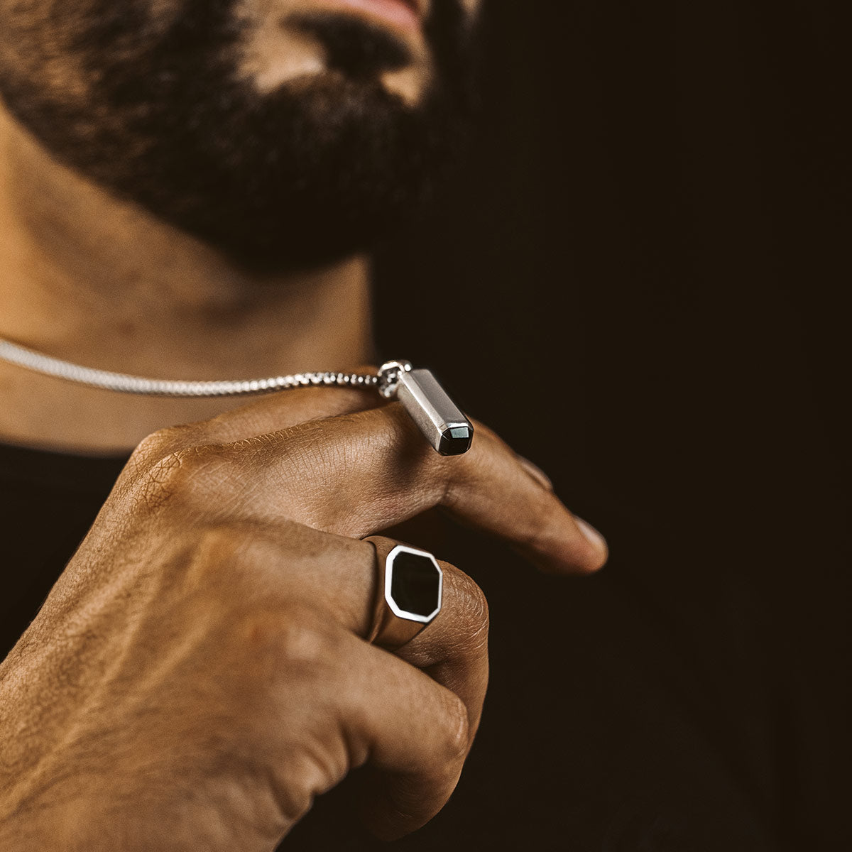 a man showing black onyx silver pendant and ring