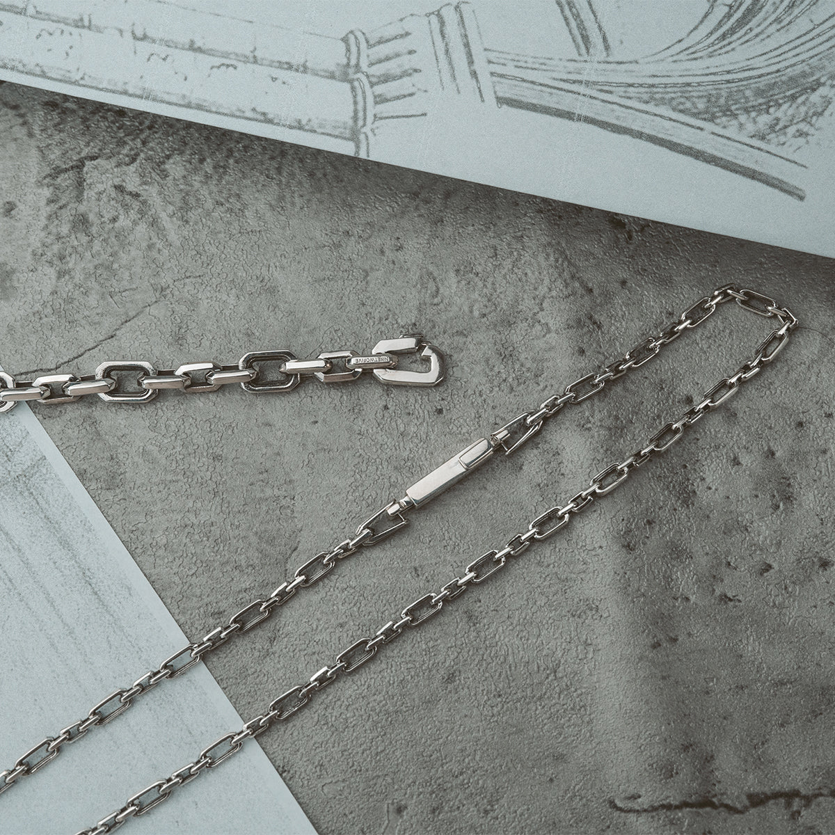 Aqdās herenarmband en Qaws sterling zilveren ketting van Ninetwofive met een op een boog geïnspireerde schets ernaast.