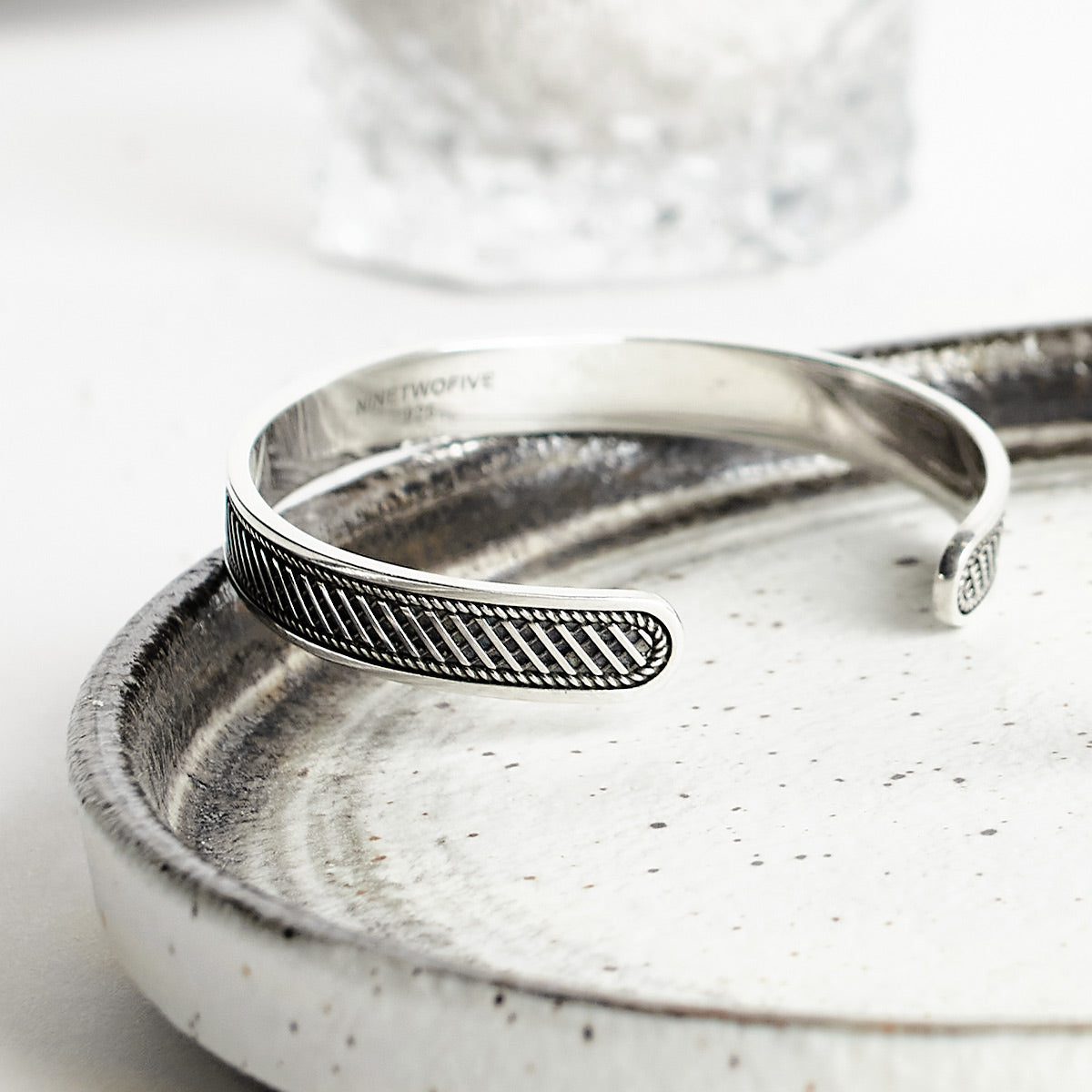 Een zilveren armband op een bord.