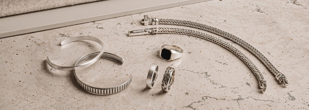 A collection of silver jewelry on a marble floor.