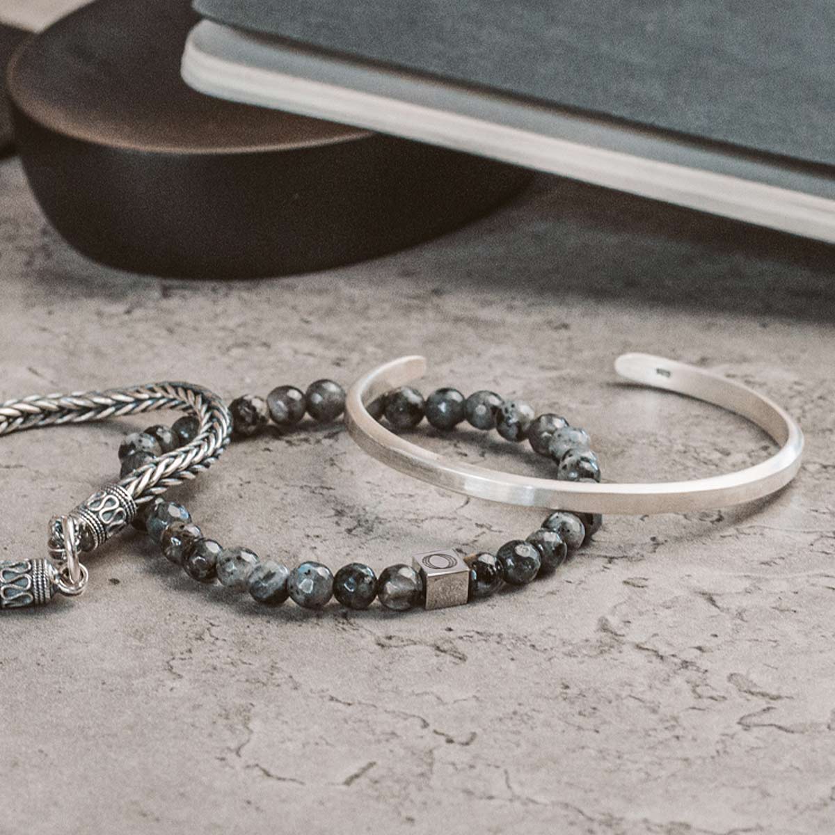 Ein Paar Silberarmbänder und ein Buch liegen auf einem Tisch.
