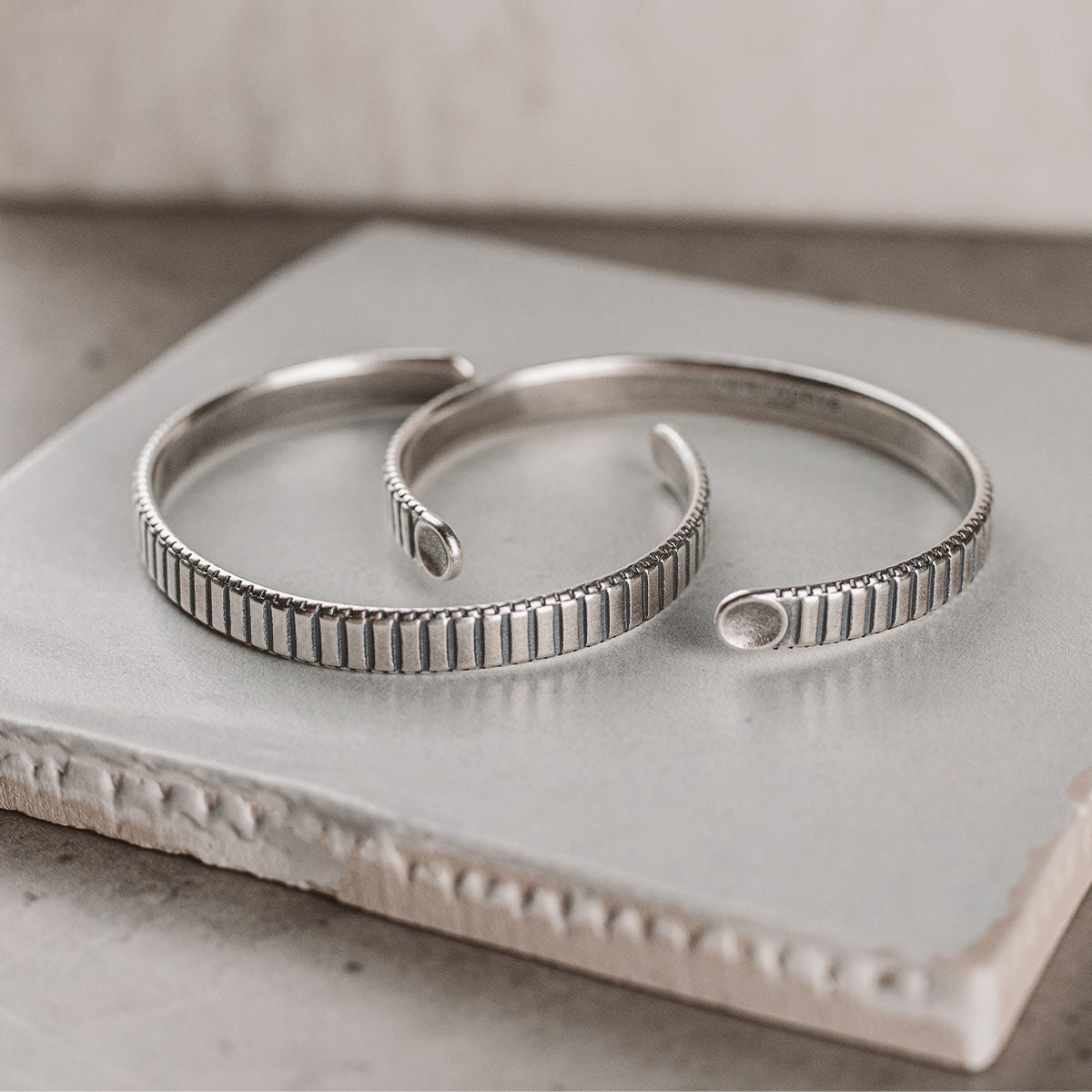 Ein Paar silberne Manschettenarmbänder auf einer Fliese.
