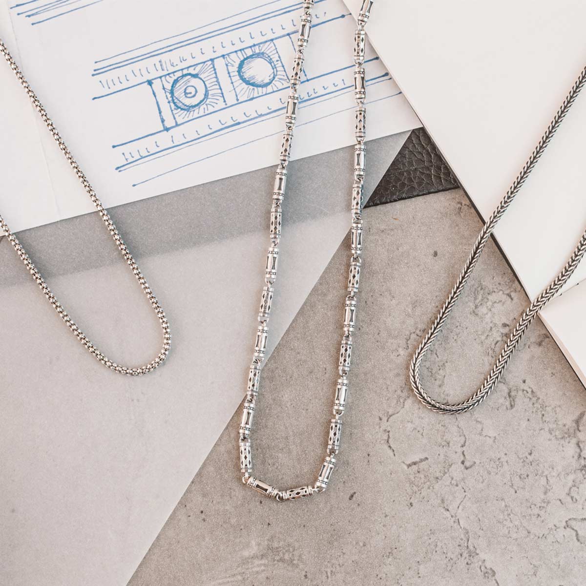 Three silver chain necklaces laying on top of a piece of paper.