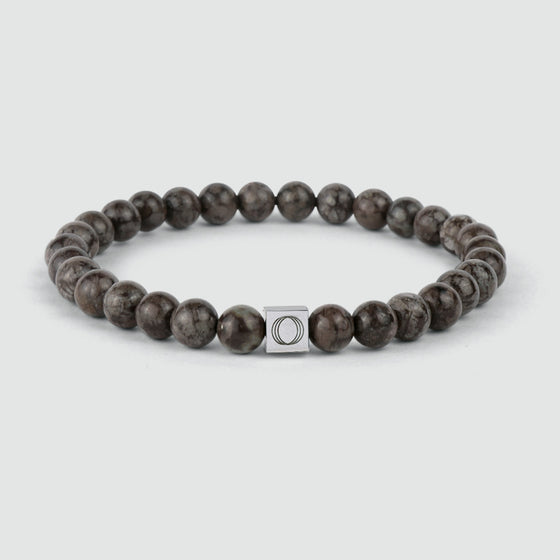 Een bruine kralenarmband van Albuna met een steenkraal in de vorm van een sneeuwvlok en het gegraveerde logo ‘Ninetwofive’.