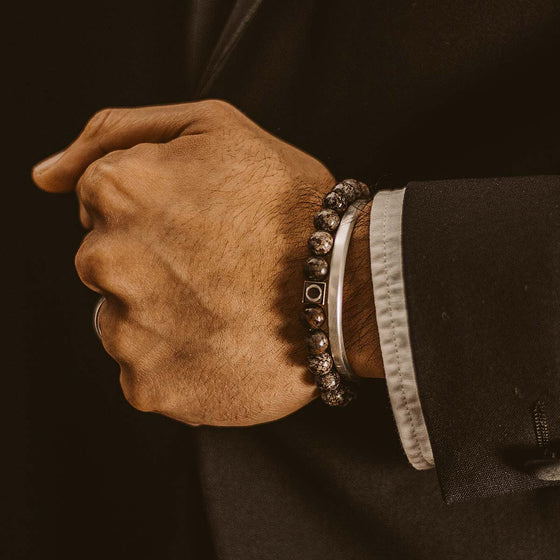 Model in a black suit displaying the Ninetwofive Albuna brown beaded men's bracelet layered with a silver cuff.