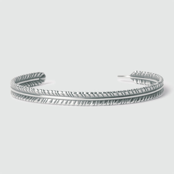 Vooraanzicht van de Zahir, een dunne heren bangle, vervaardigd uit sterlingzilver in de vorm van een veer, met een gegraveerd patroondetail.