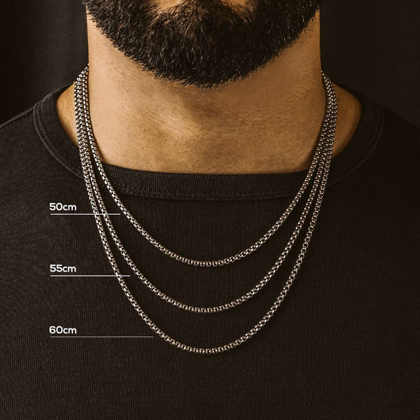 Een man in een zwart T-shirt zonder kraag, die drie verschillende soorten zilveren kettingen draagt om de verschillende lengtes te laten zien