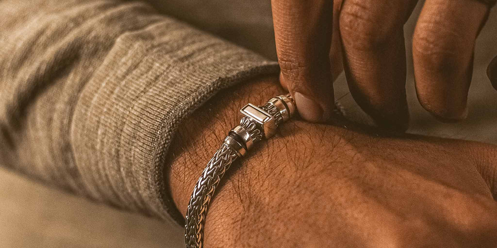 A man is holding a silver bracelet.