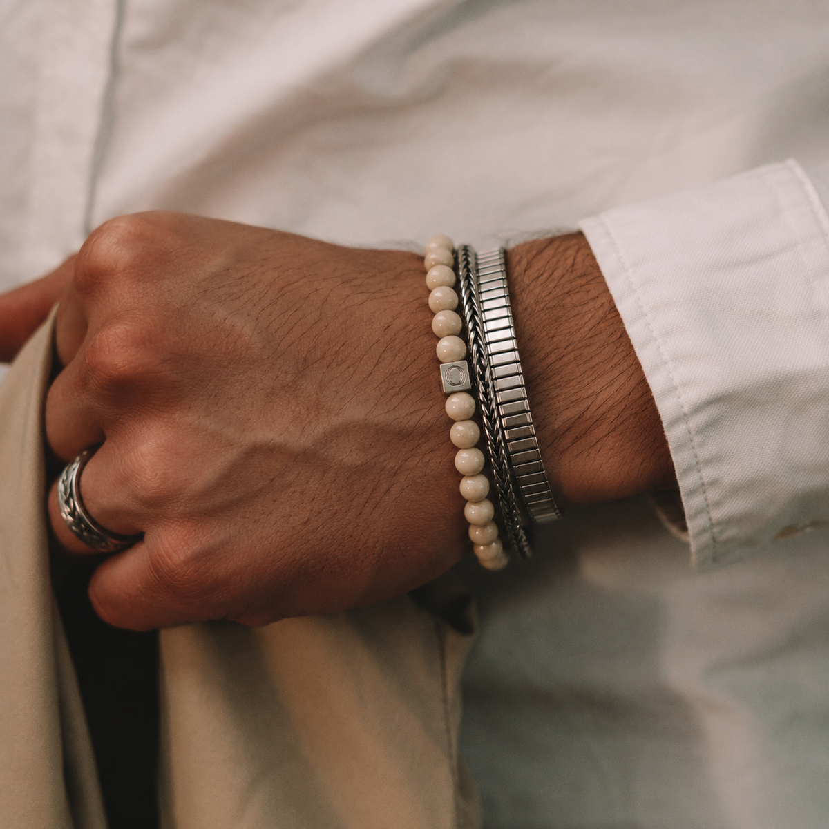 Model in a white shirt displaying the Ninetwofive Albij beige beaded men's bracelet layered with a silver cuff and ring.