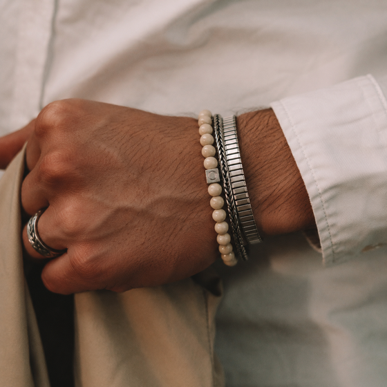 Model in a white shirt displaying the Ninetwofive Albij beige beaded men's bracelet layered with a silver cuff and ring.