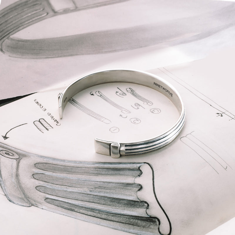 Sterling silver pillar design Arkan mens bracelet next to Ninetwofive sketch papers detailing the initial concept.