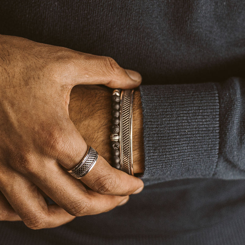 Een man in een blauwe trui draagt de Kaliq verstelbare zwarte onyx heren kralenarmband, een zilveren ring en cuff armband.