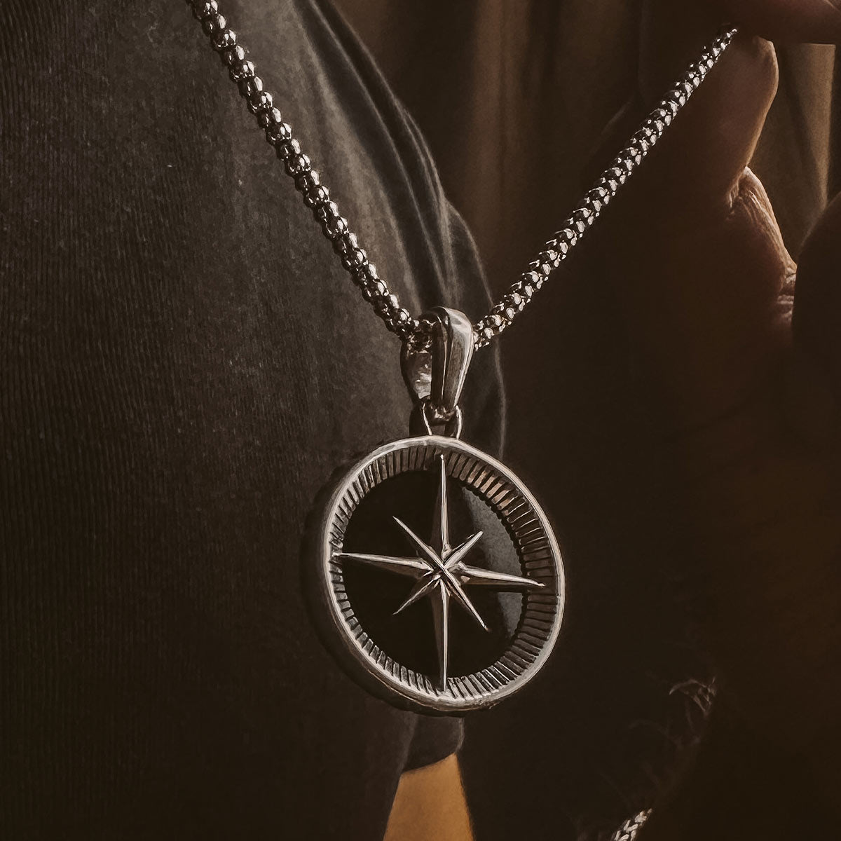 Een persoon draagt een Safar - Sterling Zilveren Onyx Kompas Hanger.