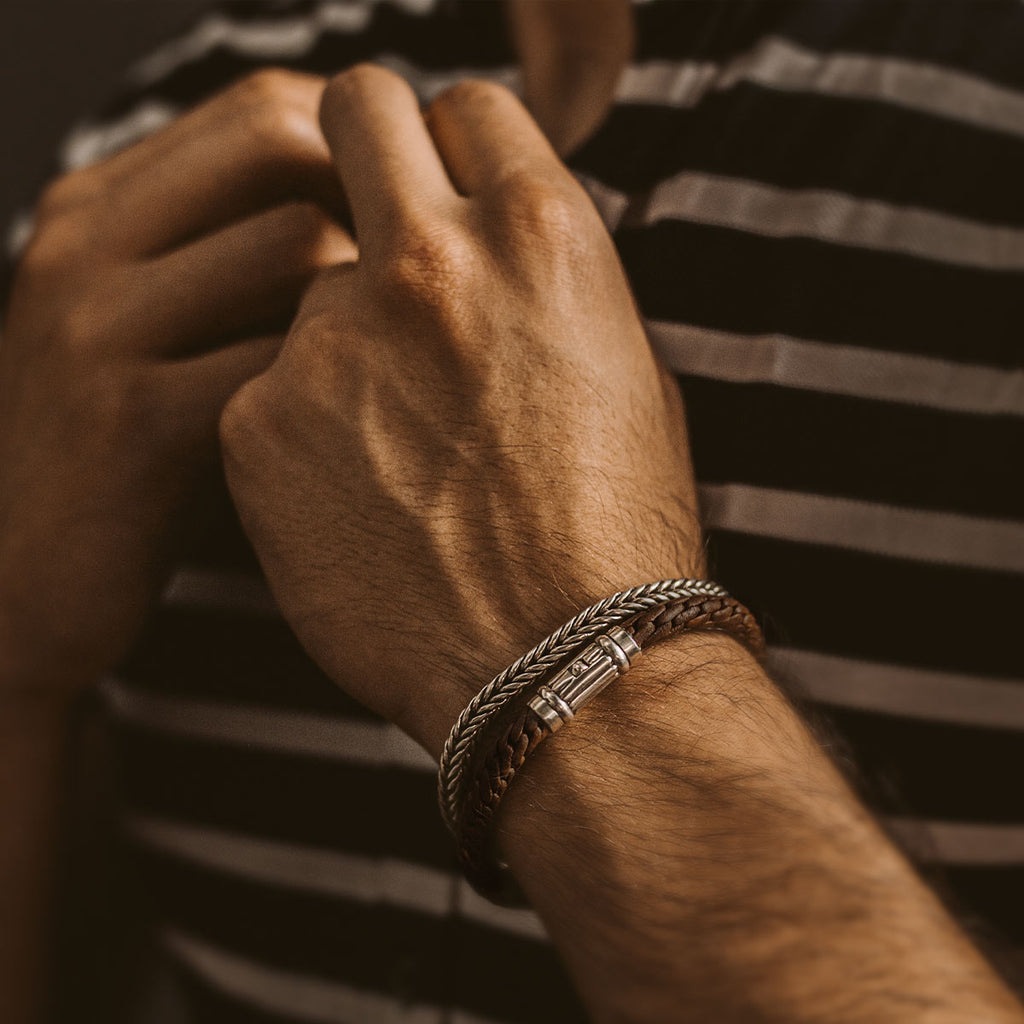 A man wearing a striped shirt and the Taissir - Genuine Brown Leather Bracelet 5mm, paired with an engraved solid silver mens bracelet.