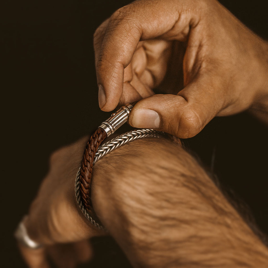 A man is putting on a Taissir - Genuine Brown Leather Bracelet 5mm.