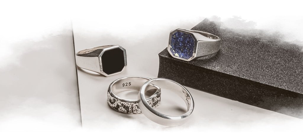 Ein silberner Ring mit einem blauen Stein ist mit einem silbernen Herrenring gepaart.