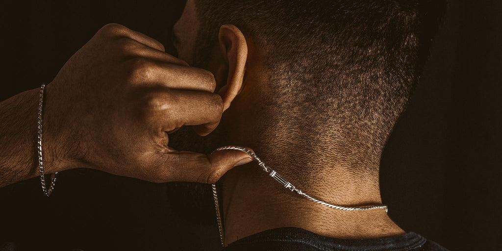 A man is putting a necklace around his neck.