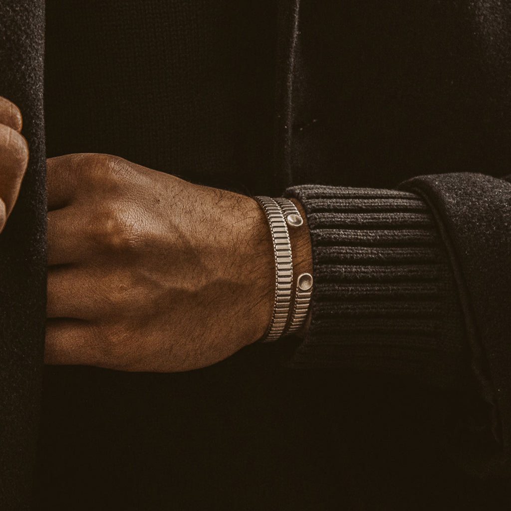 A man in a black coat is wearing a leather bracelet.