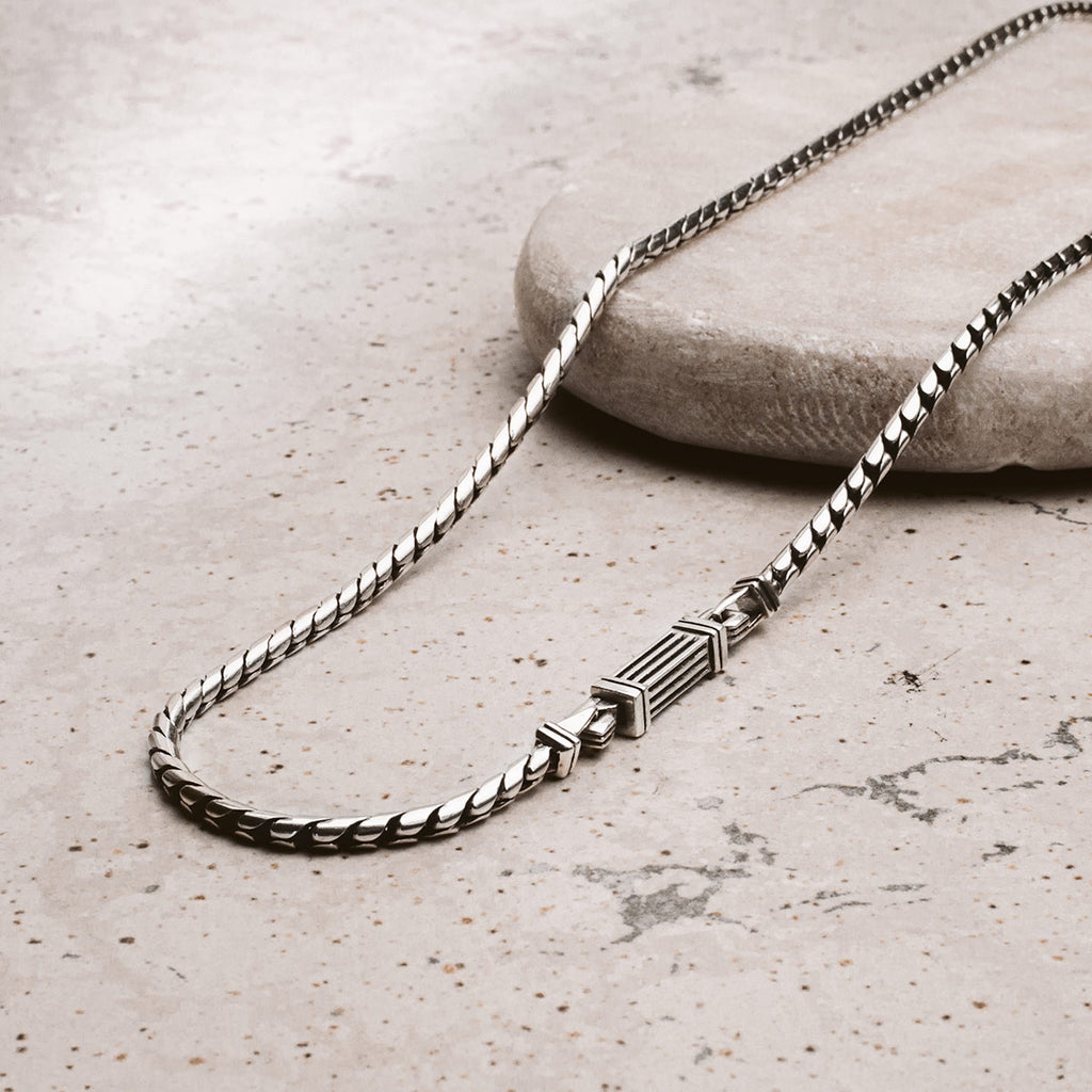 A silver chain necklace on a stone.