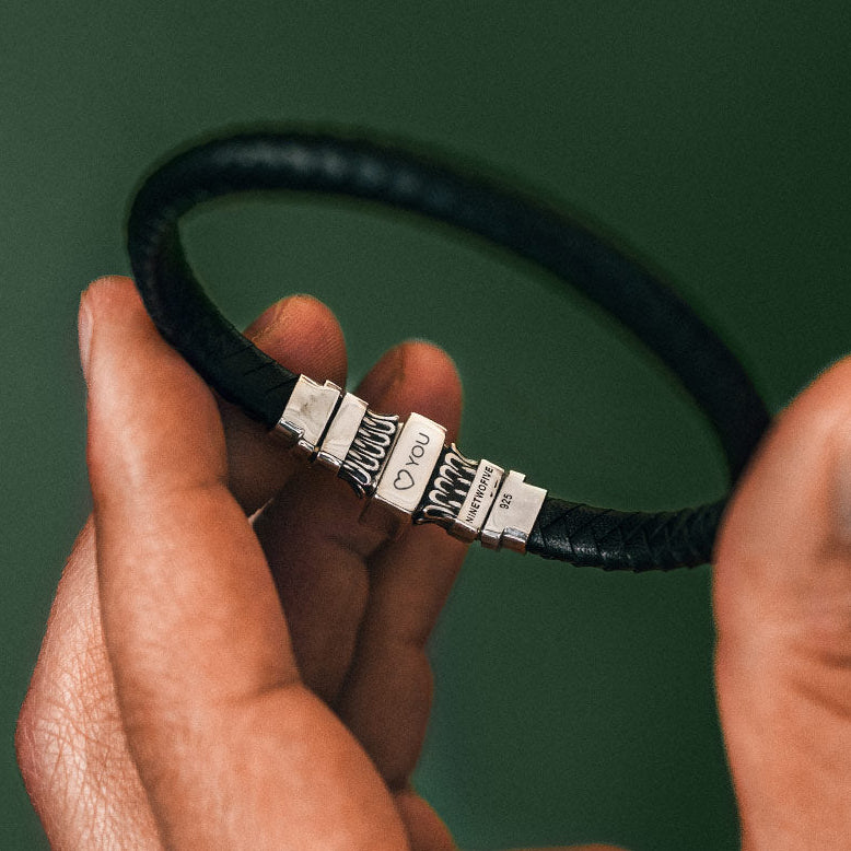 Une main tenant un bracelet en cuir noir gravé, sur fond vert