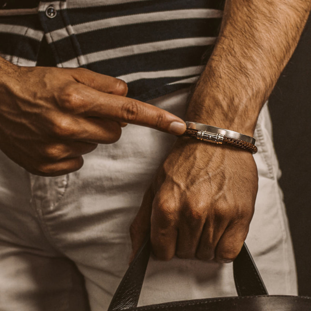 Ein Mann zeigt mit dem Finger auf eine Tasche mit einem Taissir - Authentisch Brown Leather Bracelet 5mm.