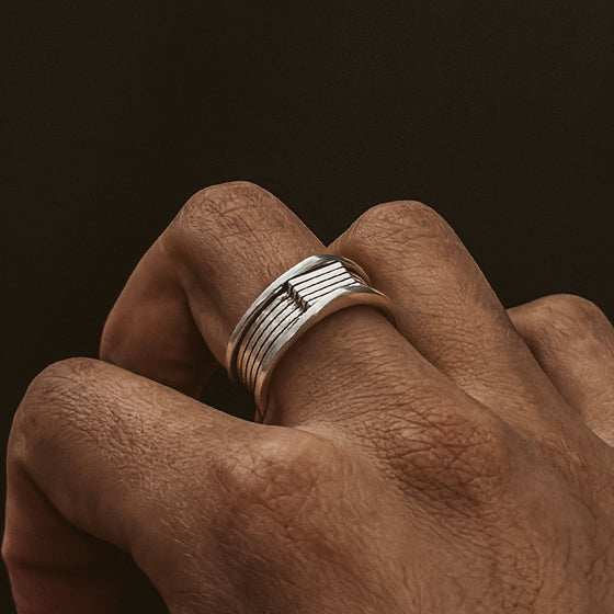 Une bague homme Yanel en argent sterling oxydé, disponible sur Ninetwofive, embellit la main d'un homme.