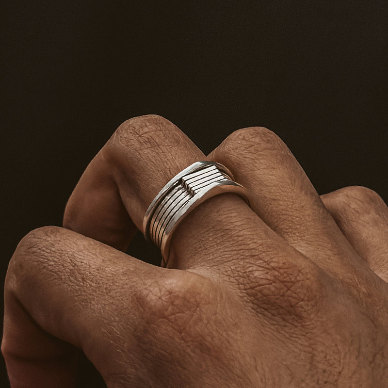 Une bague homme Yanel en argent sterling oxydé, disponible sur Ninetwofive, embellit la main d'un homme.