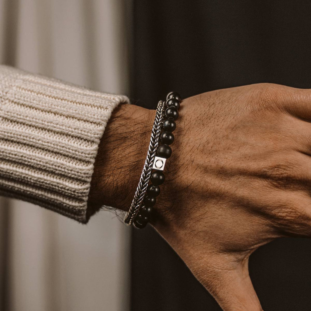 Een man draagt een Aswad - Mat Zwarte Kralen Armband 8mm van onyxsteen en een trui.