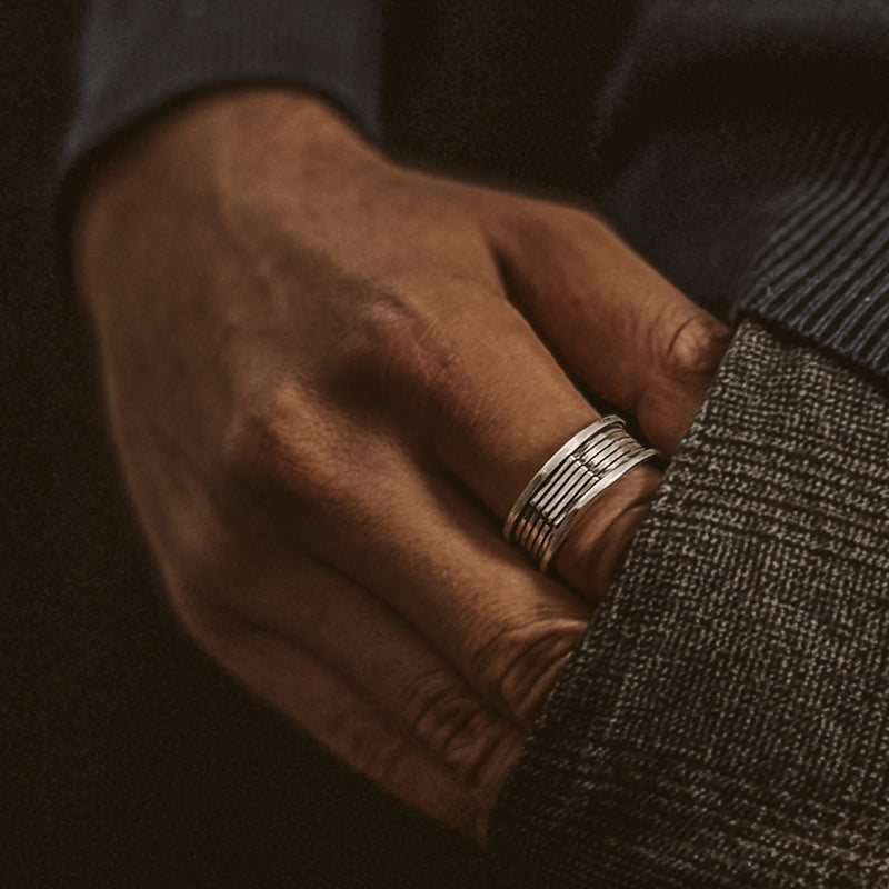 Un homme en pull bleu et pantalon gris porte la bague homme Yanel en argent, la main posée dans sa poche, Ninetwofive.