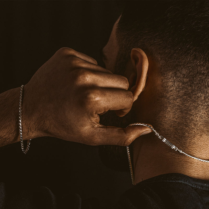 Un homme tient une chaîne en argent massif pour homme « Emir » et porte un bracelet pour homme de Ninetwofive.