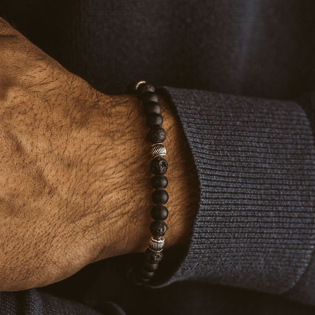 Een man draagt een Kaliq - Verstelbare Onyx Zwarte Kralen Armband in Zilver 6mm met lavasteen.