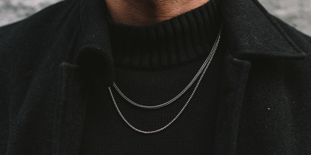 A man wearing a black coat and a silver chain necklace.