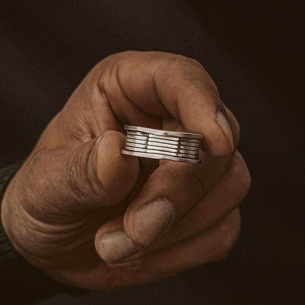 Een gegraveerde Yanel - Geoxideerd Sterling Zilveren Ring 10mm wordt elegant in de hand van een man gehouden.