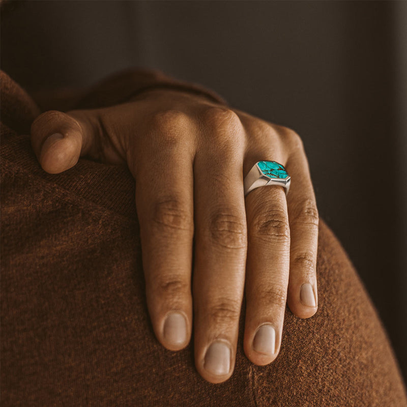 Man in a brown sweater wears the Nuri sterling silver signet ring, placing his hand onto his shoulder to show the turquoise stone.