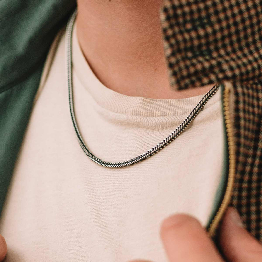 A man is wearing a necklace with a silver chain.