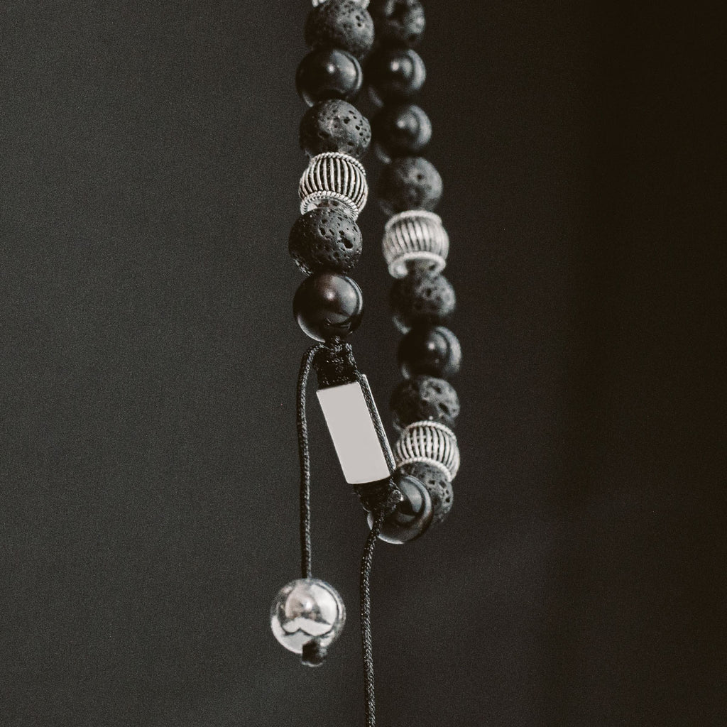 Un bracelet de perles noires et argentées suspendu sur un fond.
