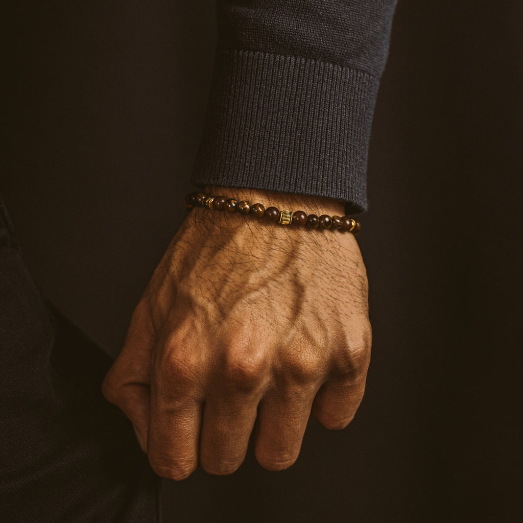 Een mannenhand versierd met een Kaliq - Verstelbare Tijgeroog Kralenarmband in Goud 6mm.