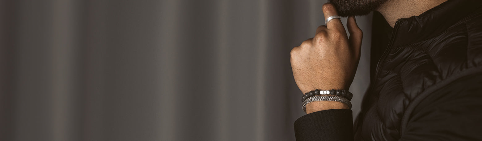 Nahaufnahme eines Mannes in schwarzer Jacke, der Silber- und Perlenarmbänder trägt, die die elegante Armbandkollektion für Männer hervorheben.