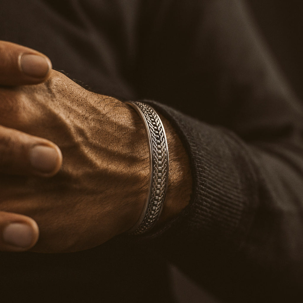 Een man draagt een zilveren armband met een patroon erop.