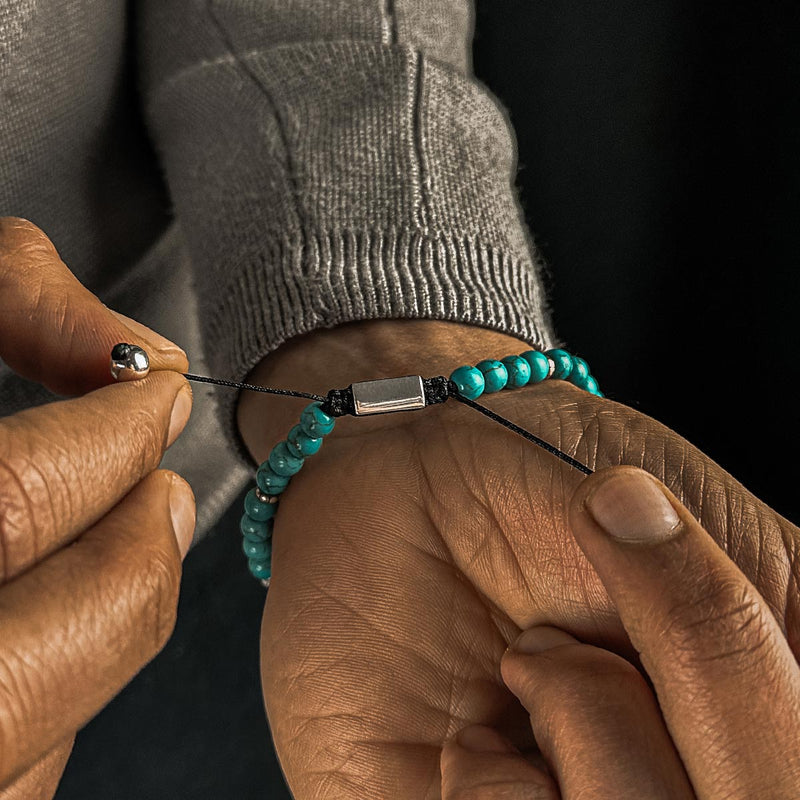 Man in grijze trui past met zijn andere hand de Nuri heren kralenarmbanden met turkoois en sterling zilver aan.