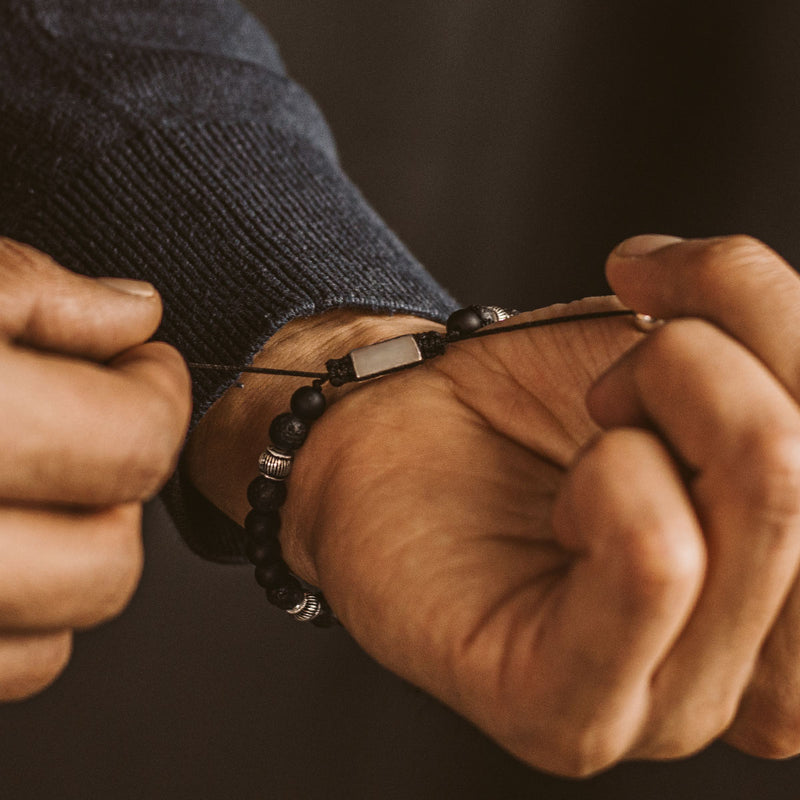 Een man in een blauwe trui stelt de Kaliq zwarte onyx heren kralenarmband af.