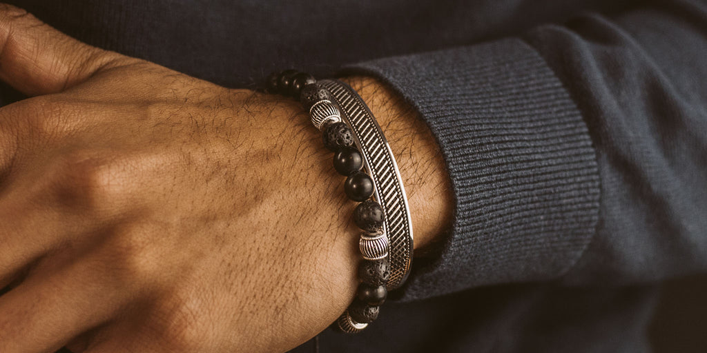 Das Handgelenk eines Mannes ist mit einem eleganten schwarzen Perlenarmband geschmückt.