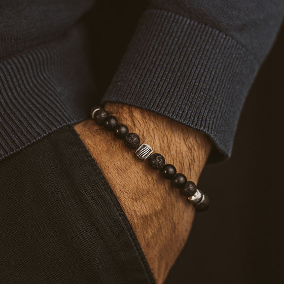 A man wearing a in silver Man in blue sweater and black trousers wears the Kaliq mens bracelet, resting his hand in his pocket, Ninetwofive.
