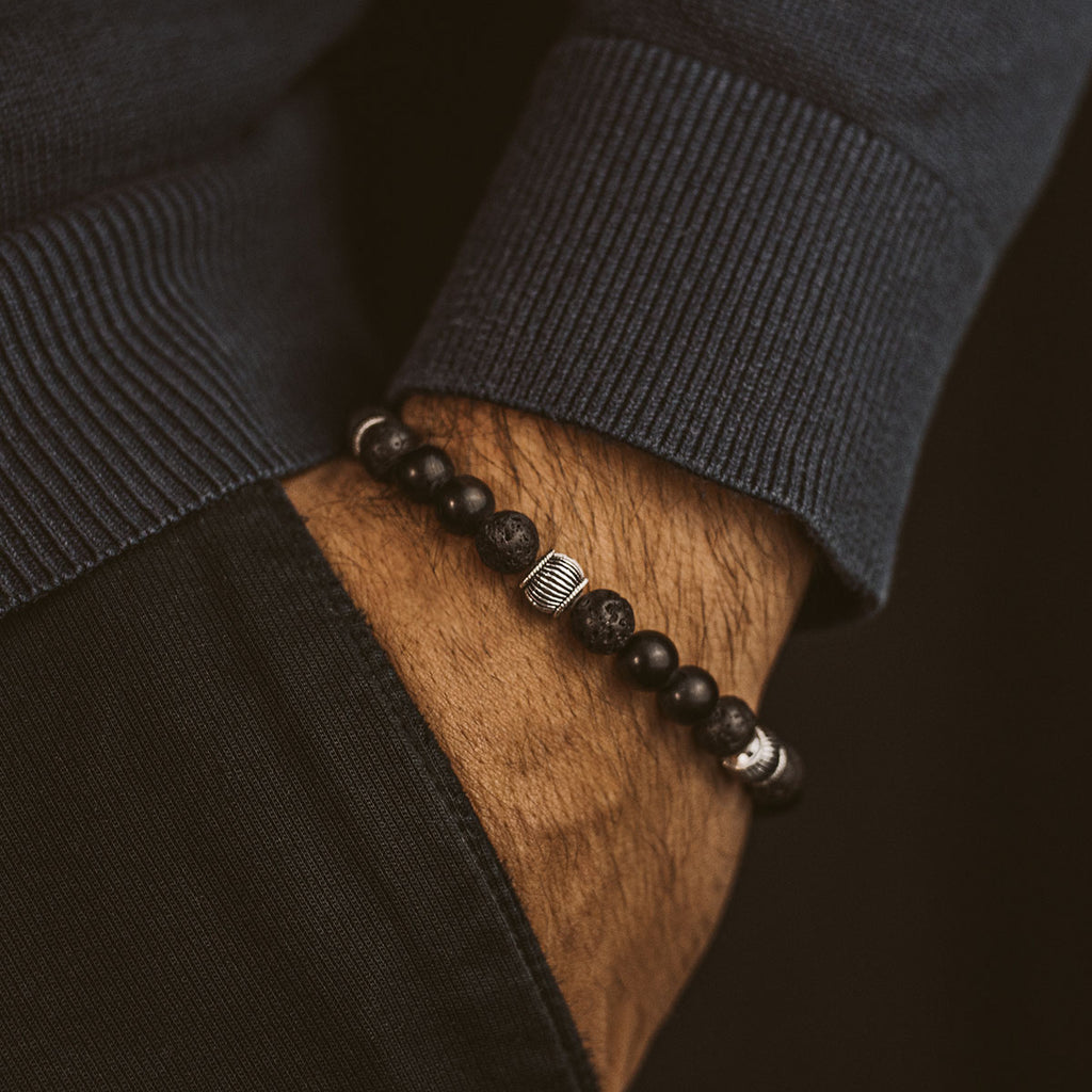 Een man draagt een Kaliq - Verstelbare Onyx Zwarte Kralen Armband in Zilver 8mm.