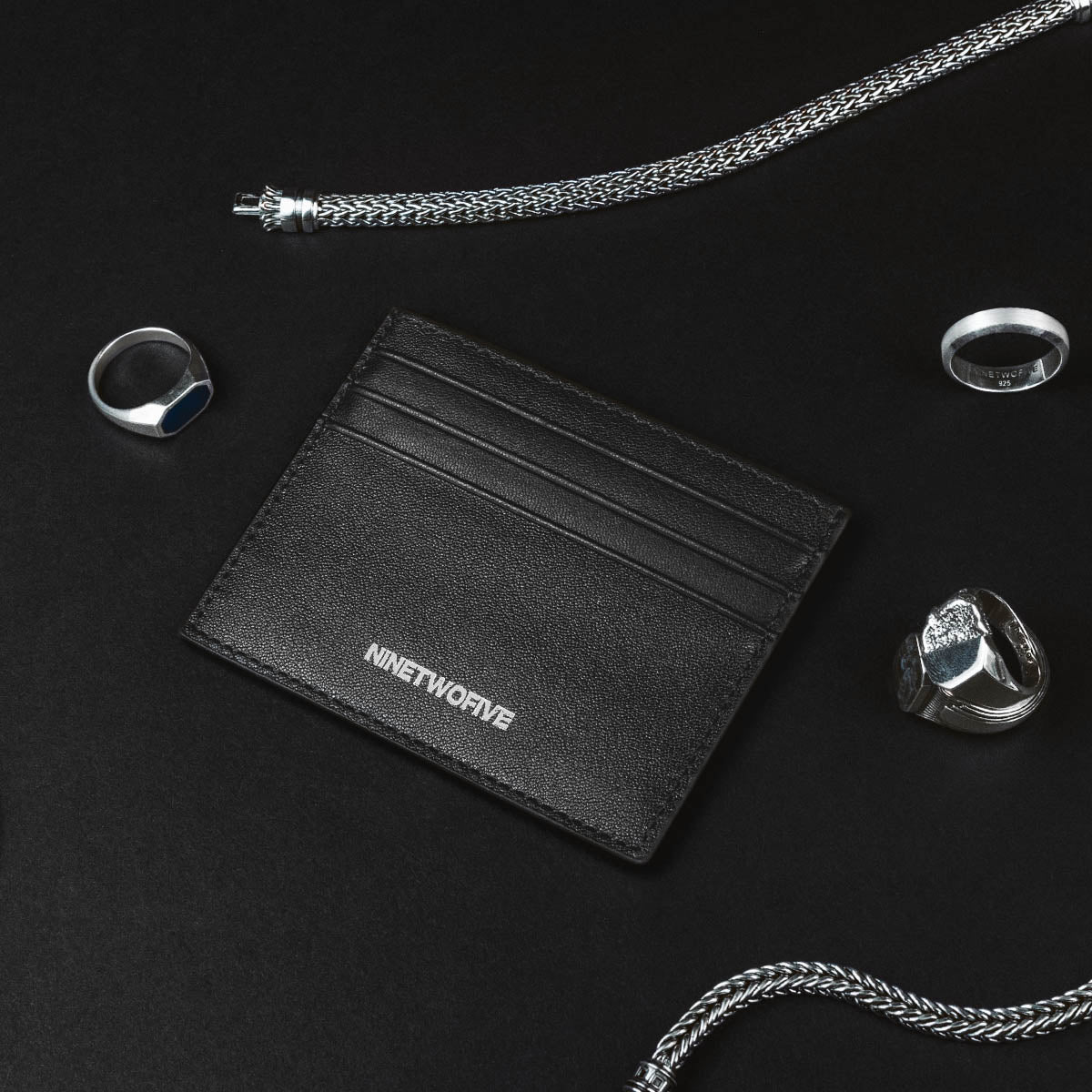 Zwartleren herenportemonnee met zegelringen en zilveren ketting van Ninetwofive op zwarte achtergrond.